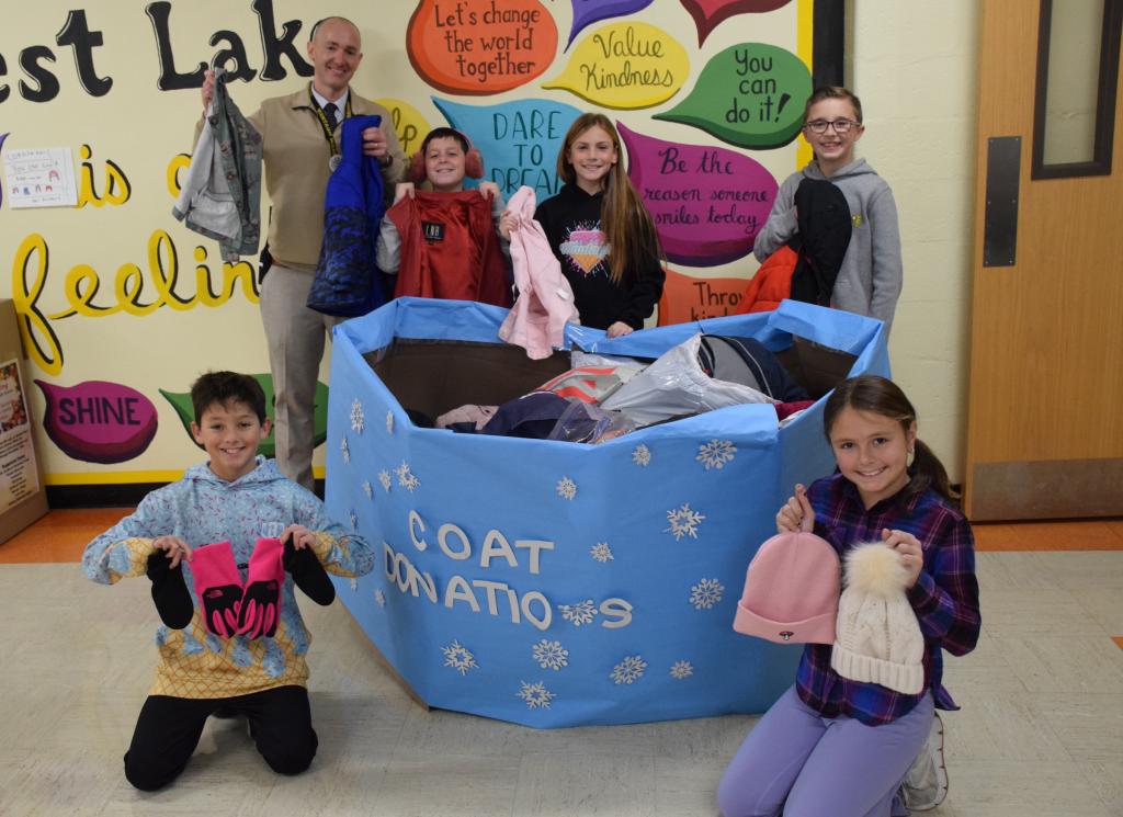 kids holding coats in front of a bin of coats